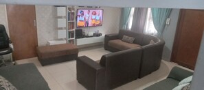 Ein Wohnzimmer mit Sofa, Hocker, Fernseher, Bücherregal und Vorhängen.