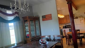 Zona pranzo con tavolo in legno, sedie, un lampadario, un armadio con vetrate e una cucina sullo sfondo.