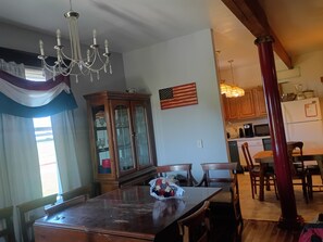 A dining area with a wooden table, chairs, a chandelier, a cabinet with glass doors, and a kitchen in the background. - The Patriot on old Route 66 40 minutes from St Louis Mo. or Springfield, Il (Staunton)