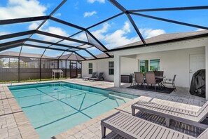 A covered outdoor swimming pool with lounge chairs and a barbecue area. - Modern Cape Coral Oasis with Saltwater Pool! (Cape Coral)