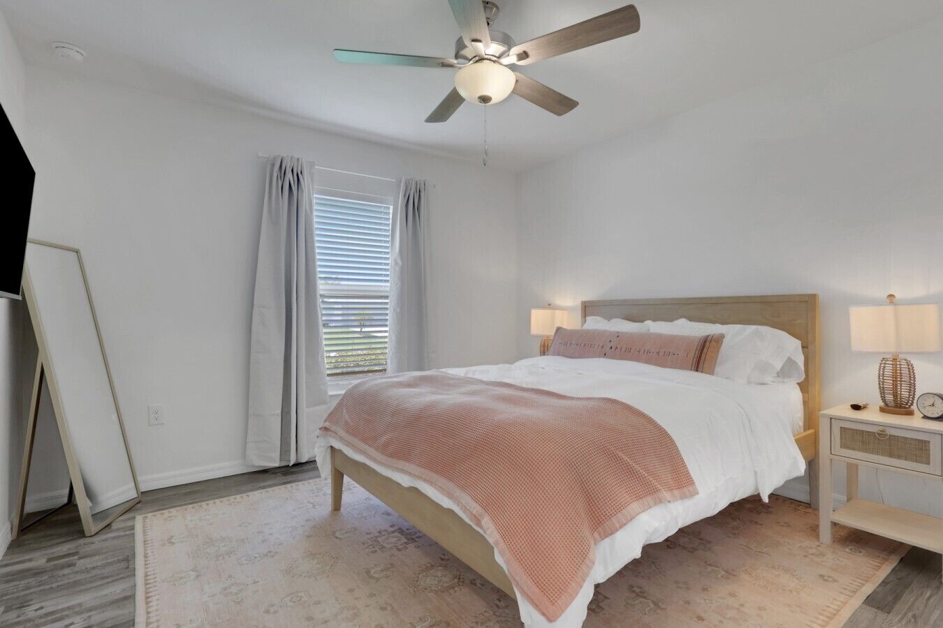 Ein Schlafzimmer mit einem Bett, einem Nachttisch mit Lampe, einem Deckenventilator und einem Fenster mit Vorhängen.