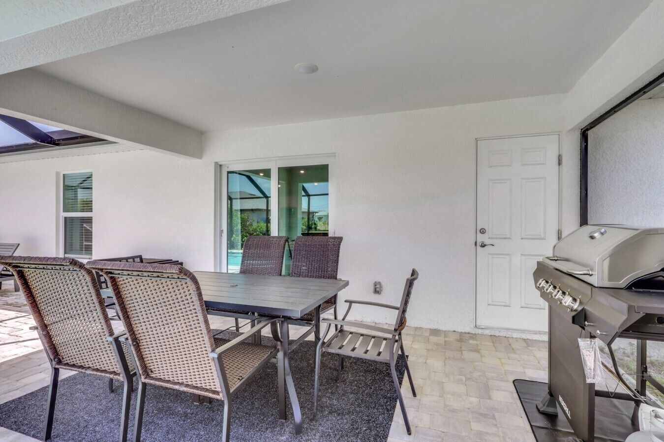 An outdoor patio with a table and chairs, a grill, and a door leading to a covered area.
