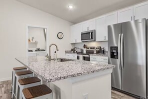 Eine moderne Küche mit weißen Schränken, einem Edelstahl-Kühlschrank, einer Mikrowelle und einer Arbeitsplatte aus Granit.
