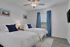Ein Hotelzimmer mit zwei Betten, einem Deckenventilator, einem Fenster mit Vorhängen und Bildern an den Wänden.