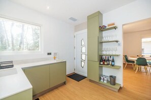 A modern kitchen with a window, a built-in shelf with glasses and bottles, and a dining area with chairs. - Villa les pins (Saint-Georges-de-Didonne)