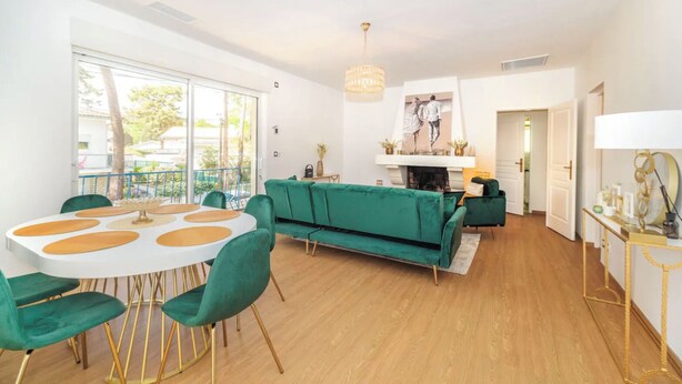A modern living room with a green sofa, a white dining table with gold accents, and a fireplace. - Villa les pins (Saint-Georges-de-Didonne)