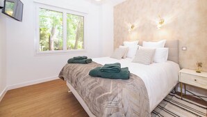 A bedroom with a bed, a window, a bedside table, and a wall-mounted light fixture. - Villa les pins (Saint-Georges-de-Didonne)