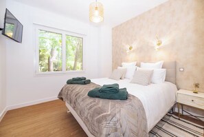 A bedroom with a bed, a window, a bedside table, and a wall-mounted light fixture. - Villa les pins (Saint-Georges-de-Didonne)