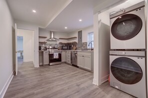 A modern kitchen with built-in appliances, a large washer and dryer, and a view to the dining area.