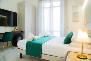 Habitación de hotel con cama, escritorio, televisión y ventana con cortinas.