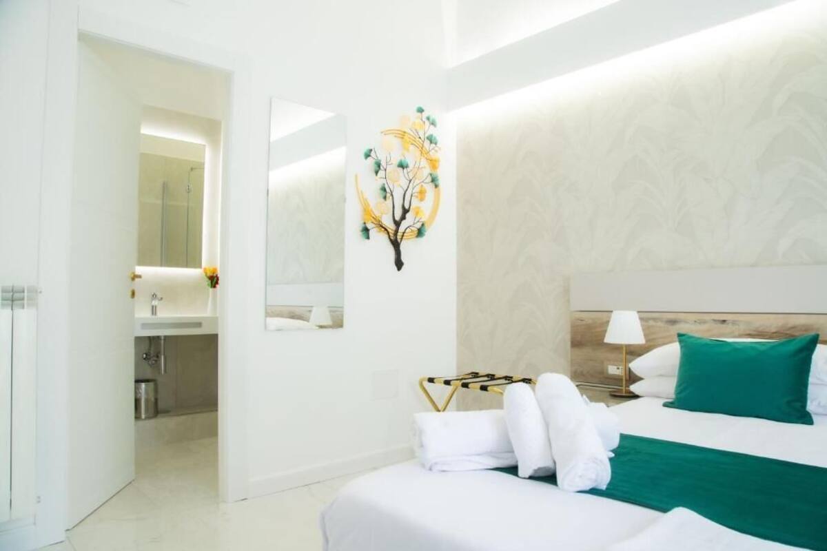 A hotel room with a bed, a mirror, a wall-mounted artwork, and a bathroom visible through an open door.