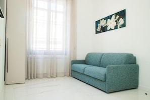 Una habitación con un sofá color turquesa, una puerta blanca y una ventana con cortinas de gasa.