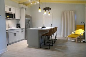 A modern kitchen with white cabinets, a central island, and bar stools. - Tropical Beach Cottage-Steps to the Beach-Short Walk to Siesta Key Village (Siesta Key)