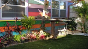 Une maison aux couleurs vives, avec un petit jardin, une table en bois et des chaises.