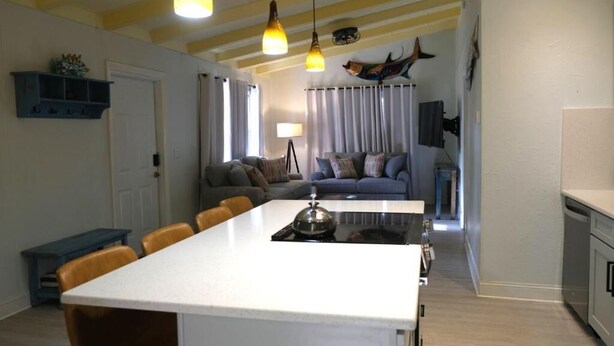 Une cuisine moderne avec un îlot central, un coin repas avec des chaises et un salon avec un canapé et des rideaux.