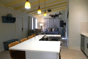 Une cuisine moderne avec un îlot central, un coin repas avec des chaises et un salon avec un canapé et des rideaux.