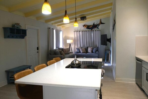 A modern kitchen with a central island, a dining area with chairs, and a living room with a sofa and curtains. - Tropical Beach Cottage-Steps to the Beach-Short Walk to Siesta Key Village (Siesta Key)