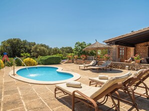 Ein Swimmingpool mit Liegestühlen und einer Pergola, umgeben von Steinmauern und Topfpflanzen.