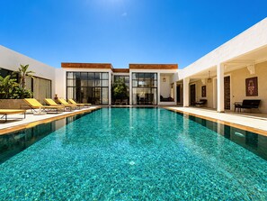 A modern pool area with clear water, sun loungers, and a building with large windows.