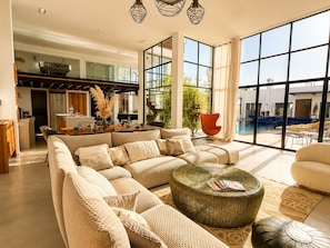 A spacious living area with a large sofa, a coffee table, and a view of an outdoor swimming pool.