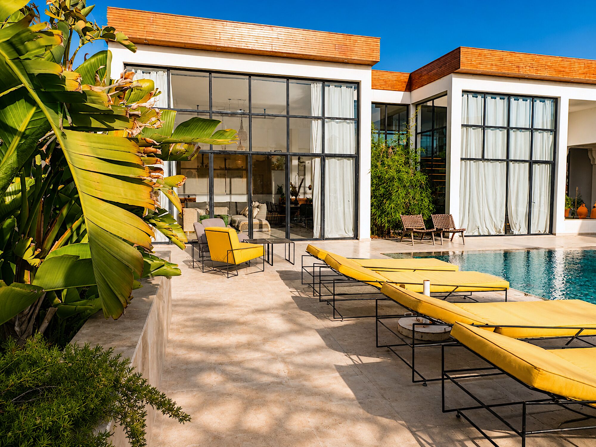 Un espace piscine moderne avec des chaises longues, un coin repas et de grandes fenêtres.
