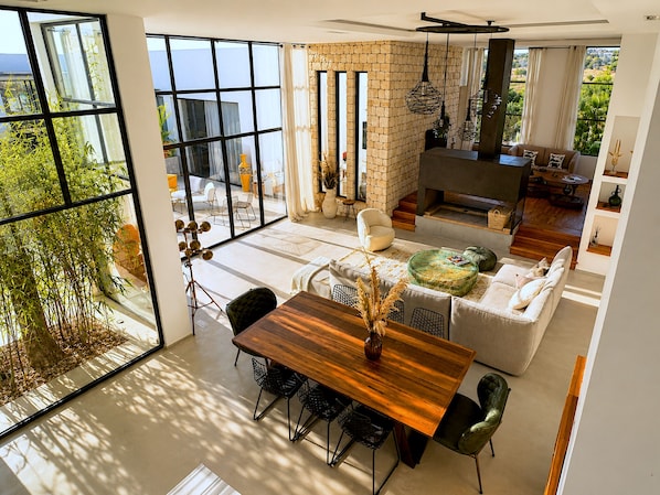 A spacious living area with a large window, a fireplace, and a dining table with chairs.