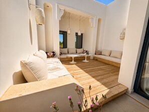 Un espace extérieur lumineux, aménagé pour se détendre, avec une terrasse en bois, des coussins blancs et des lanternes suspendues.