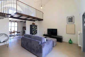 A spacious living area with a sofa, a TV, a dining table with chairs, a staircase, and artwork on the walls. - Riad del Capo by LoveSud (Castrignano del capo)