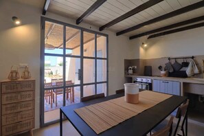 A kitchen with a stove, oven, and cabinets, a dining table with a placemat, wicker storage, and a sliding glass door leading outside. - Riad del Capo by LoveSud (Castrignano del capo)