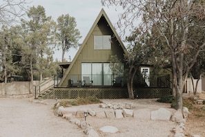 Une maison en forme de triangle avec une structure en A, dotée d’un porche, de grandes fenêtres et d’une cour clôturée.