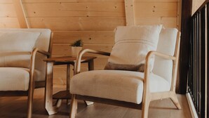 Interno di una baita in legno con due poltrone imbottite, un tavolino e una pianta in vaso.