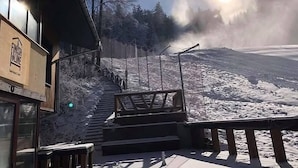 A building with a staircase leading up to a platform, surrounded by snow-covered ground and trees. - Finish Line Guest House (Samokov)