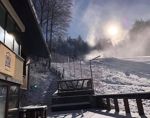 A building with a staircase leading up to a platform, surrounded by snow-covered ground and trees.