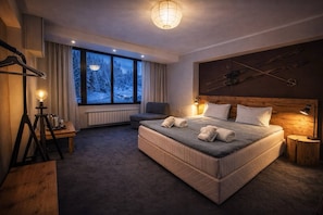 Una habitación de hotel acogedora con una cama grande, vistas a un paisaje nevado, un esquiador en la pared y una lámpara en la mesita de noche.