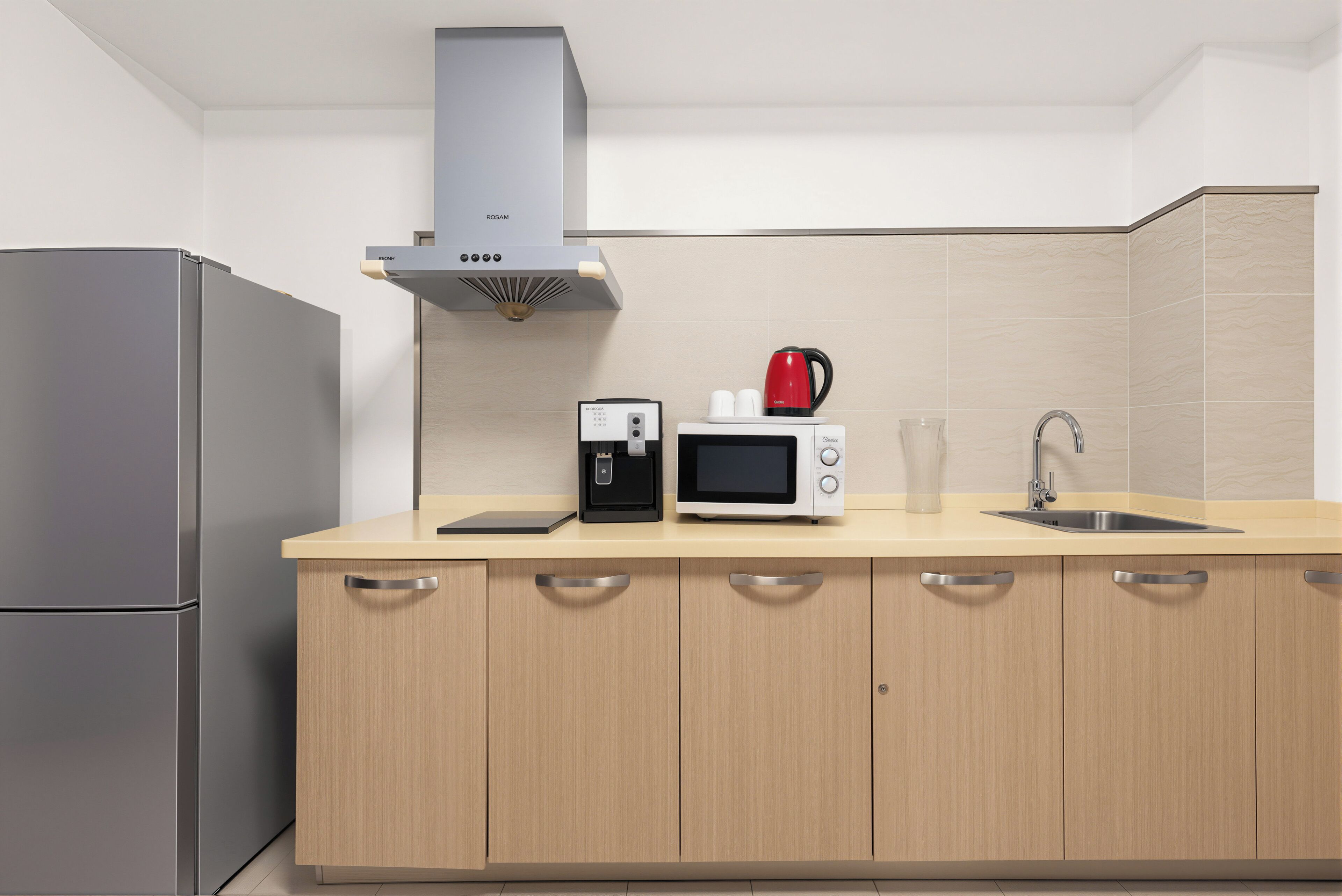 Una cocina moderna con un refrigerador de acero inoxidable, cafetera, microondas y pileta.