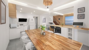 A modern kitchen with white cabinetry, a wooden dining table, and a hanging light fixture.