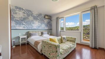 A bedroom with a large bed, a sofa, a nightstand, and a wall-mounted air conditioner.