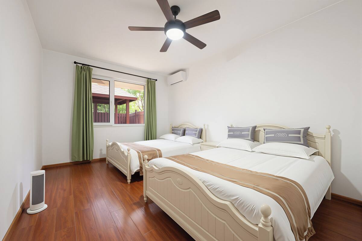 Ein Schlafzimmer mit zwei Einzelbetten, einem Deckenventilator, einem Fenster mit Vorhängen und einer Heizung.