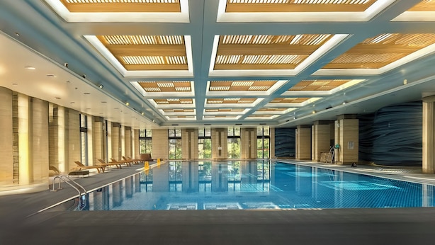 An indoor swimming pool with a modern ceiling design, large windows, and a clear view of the outdoors.