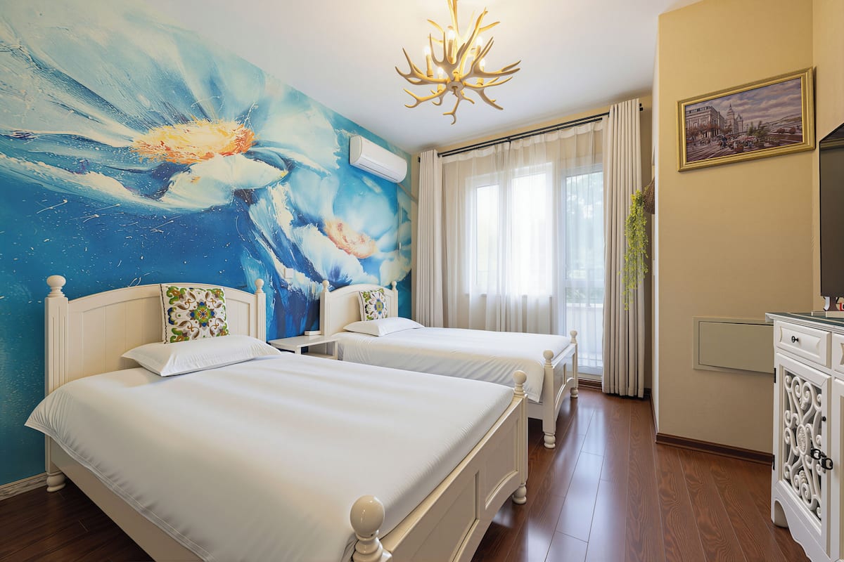 Ein Hotelzimmer mit zwei Betten, einer Kandelaber, einem Gemälde und Blick auf die Stadt.