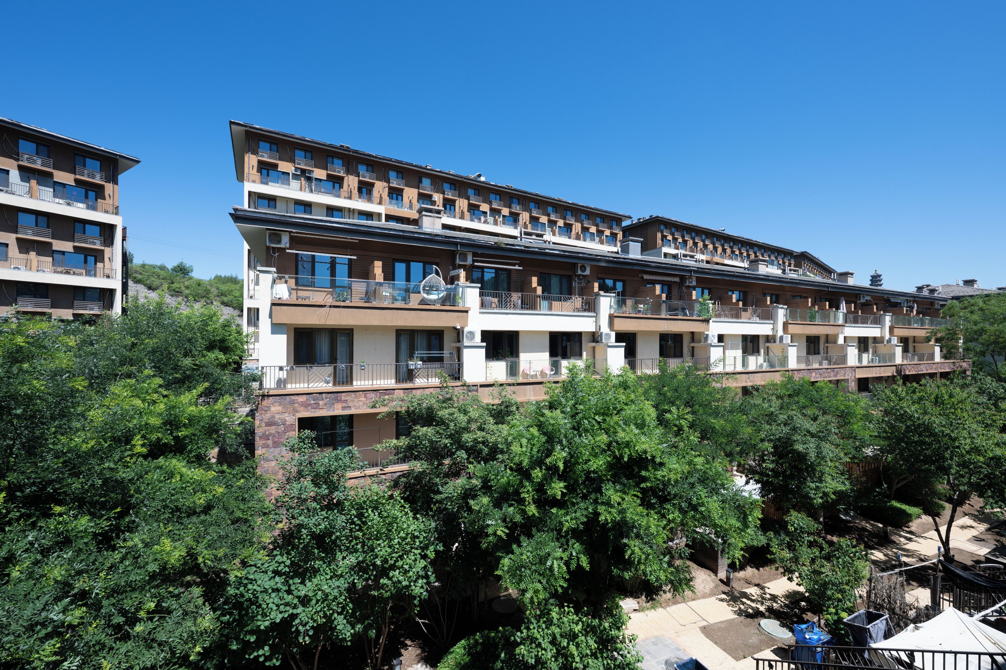 A multi-story hotel with balconies, a flat roof, and surrounded by trees.