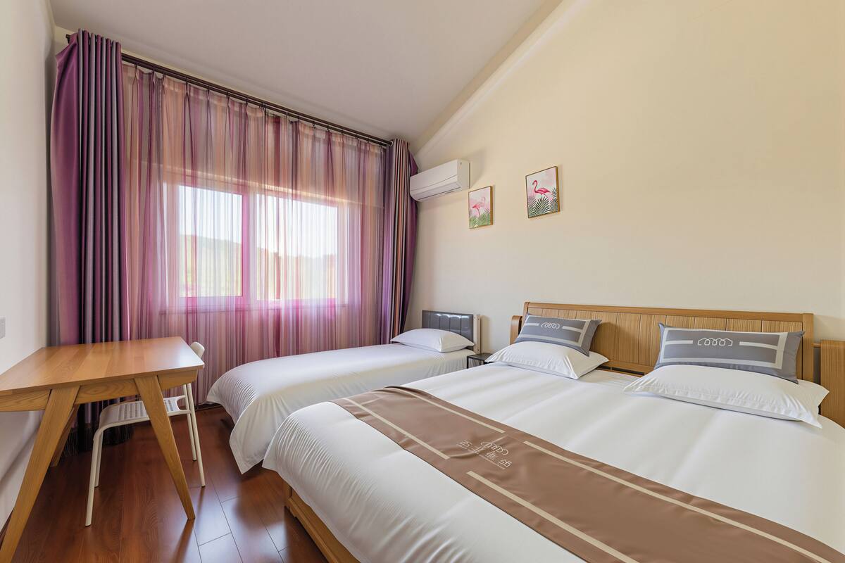 Ein Hotelzimmer mit zwei Betten, einem Schreibtisch und einem Fenster mit Vorhängen.