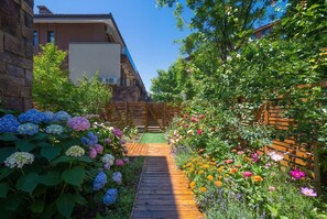 A garden pathway leading to a wooden deck, surrounded by lush greenery and flowering plants.