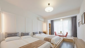 A hotel room with two beds, a desk, a chair, a small table, and a window with curtains.