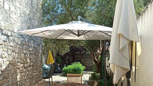 Een houten terras met een tafel, stoelen en een parasol, met een stenen muur ernaast.