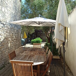 A wooden deck with a table and chairs, an umbrella, and a stone wall. - Large, comfortable house close to the beach (Rivedoux-Plage)