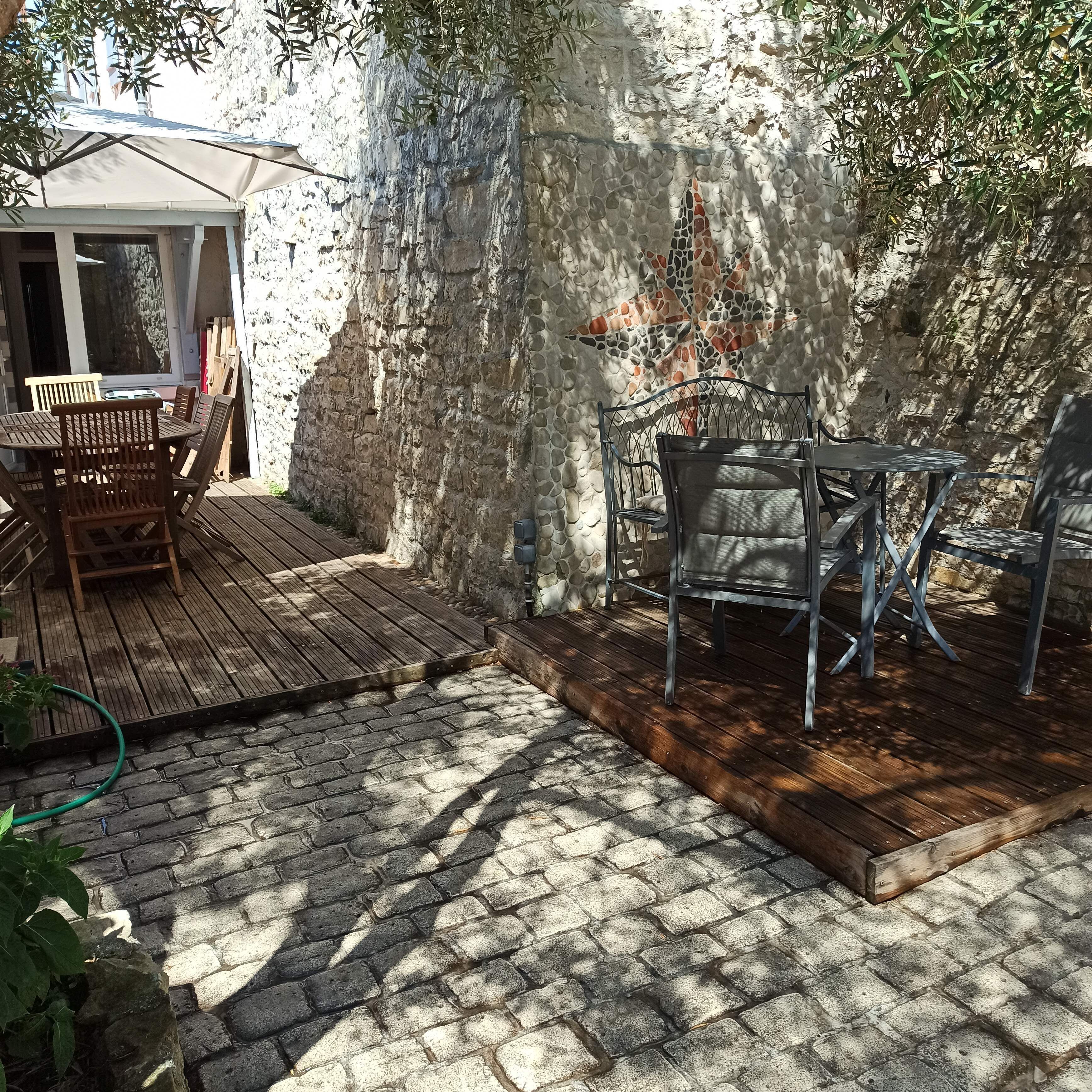 A patio with a wooden deck, a stone wall, and a metal chair.