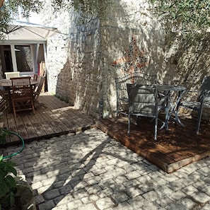 A patio with a wooden deck, a stone wall, and a metal chair. - Large, comfortable house near the beach (Rivedoux-Plage)