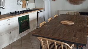 Een moderne keuken met een houten tafel, stoelen, een fornuis, oven, koelkast en een grote hanglamp.
