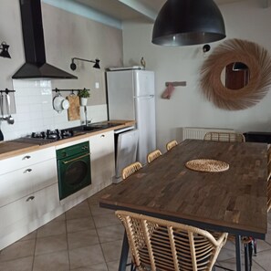 A modern kitchen with a wooden table, chairs, a stove, oven, refrigerator, and a large pendant light. - Large, comfortable house close to the beach (Rivedoux-Plage)
